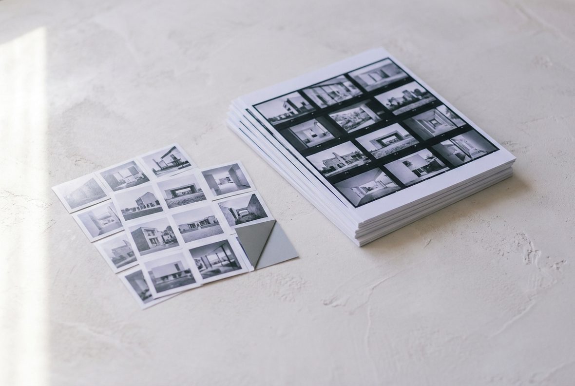 Contact sheets and a fanned grid of near-identical thumbnail prints on a pale plaster surface, one turned face down.